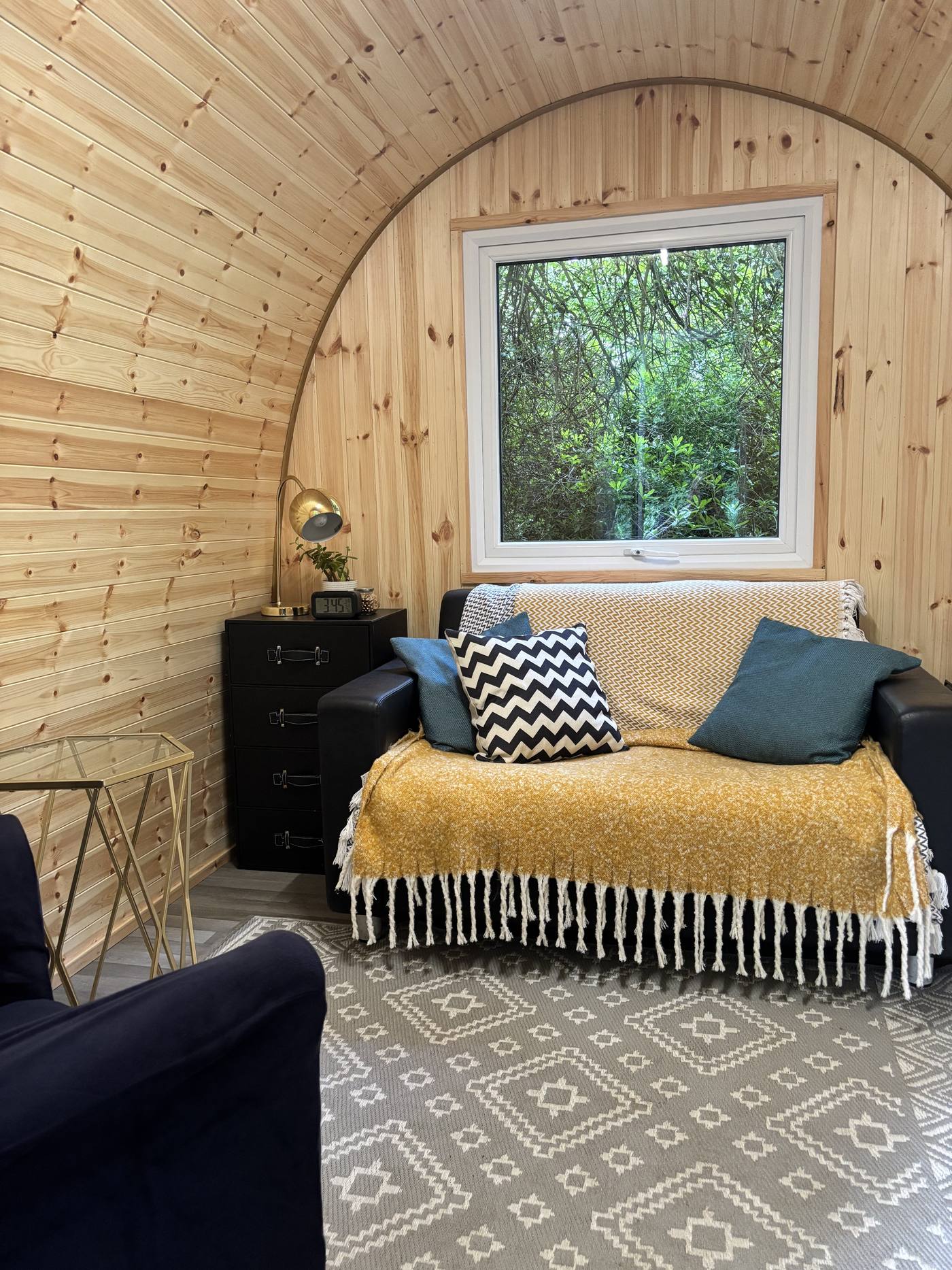 The warm, timber-lined interior of a Vicarage Gardens pod, with an armchair, sofa and a window onto the trees
